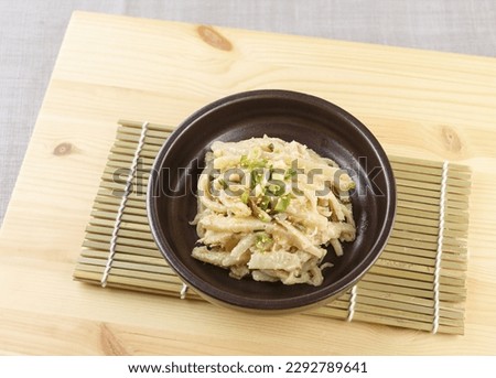 Close-up of seasoned balloon flower roots with chives and sesame seed on brown dish and sushi roller mat, South Korea
