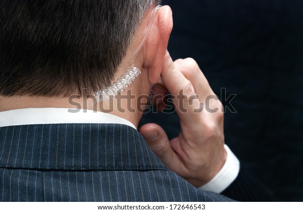Close-up of a secret service agent listening to\
his earpiece, behind.