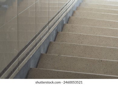 A close-up of a section of a granite staircase with a metal handrail, showcasing the steps textured surface and the reflective tiles on the wall, hinting at a well-maintained indoor setting, possibly - Powered by Shutterstock