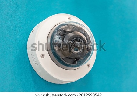 Close-up security camera in controlled lighting environment, white glossy dome design with small speaker grille visible on the side, emphasizing reflective surfaces and product features, clean