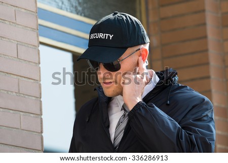 Close-up Of Security Guard Standing In Front Of The Entrance Listening To Earpiece