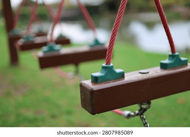 Close-up selective focus of empty wooden playground swings with red ropes hanging in a quiet park area