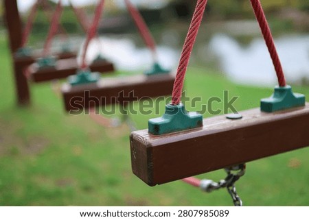 Close-up selective focus of empty wooden playground swings with red ropes hanging in a quiet park area