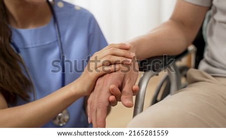 closeup with selective focus of hands of nursing aide holding and patting winkled hand of a patient on wheelchair. Domiciliary care for sick elderly people concept