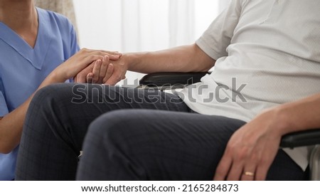 closeup with selective focus of hands of nursing aide holding and patting winkled hand of a patient on wheelchair. Domiciliary care for sick elderly people concept
