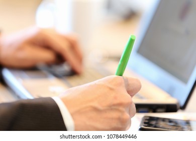 close-up selective focus on man right hand holding pen to write memo on sticky note while using laptop searching for information - Powered by Shutterstock