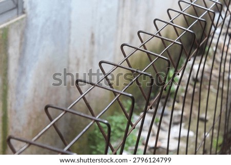 Close-up selective focus of a rusty wire mesh fence with a blurred concrete wall background.