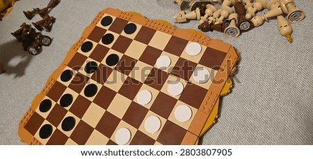 Close-up selective focus shot of a chess board and chess pieces entirely constructed from plastic building bricks. The brown and beige pieces, including the king, queen, rooks, and pawns, are arranged on a checkered brick board over a soft indoor couch background. This image perfectly illustrates strategy, logic, intellect, board games, building block hobbies, smart entertainment, and educational activities for kids and adults.
