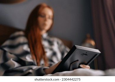Closeup selective focus shot of sad young woman lying on bed holding photo in frame and crying looking at picture, touching photograph with love. Unhappy female looking to photo with nostalgic feeling