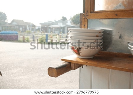 A Close-Up Selective Focus Shot of Stacked Traditional Indonesian Rooster Ceramic Bowls on a Wooden Food Cart Sideboard.