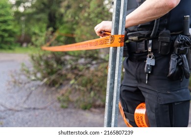 Closeup selective focus view on belt of local police officer closing a main road with tape in aftermath of storm, blurry uprooted tree in background.
