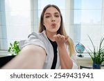 Close-up selfie portrait of young cheerful woman looking at web camera