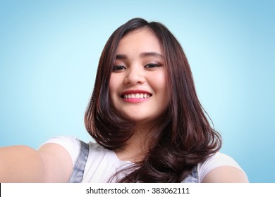 Close-up self-shot portrait of cute Asian teenage girl smiling over blue background