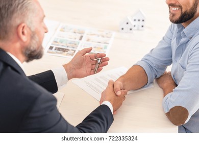 Close-up Of Seller Shaking Hand And Giving Keys To Smiling Customer Who Bought House