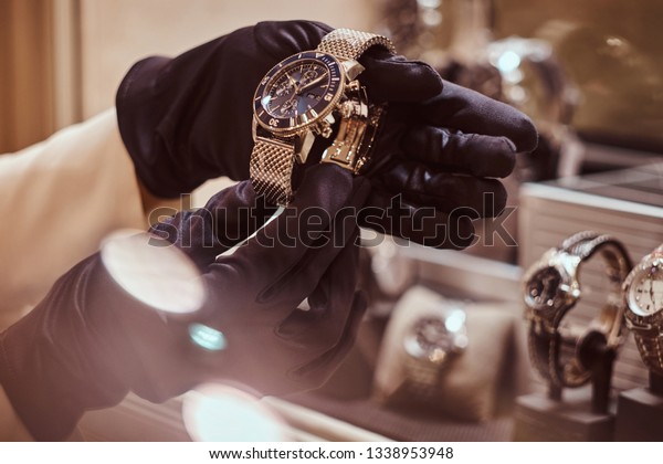 Close-up of the seller\'s hands in gloves shows the\
exclusive men\'s watch from the new collection in the luxury jewelry\
store