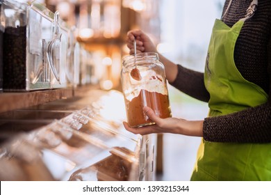 Close-up of the seller's hands holding a jar of spice near the bulk dispensers in an organic food store