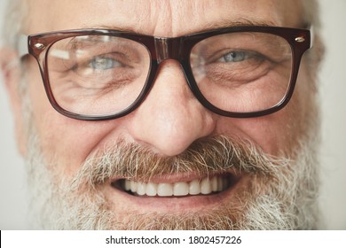 Close-up of senior bearded man in eyeglasses smiling at camera