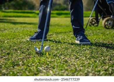 Close-up of a senior golfer's legs as they stand with the golf club poised to hit the ball resting on the tee. The stance emphasize focus and readiness for the initial drive on the course - Powered by Shutterstock