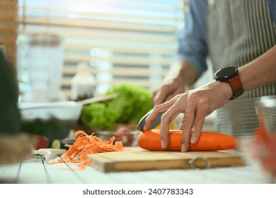 Closeup senior man chopping fresh carrot on board preparing a healthy salad in kitchen. - Powered by Shutterstock