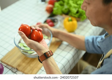 Closeup senior man holding tomatoes while cooking healthy vegan food in kitchen. - Powered by Shutterstock