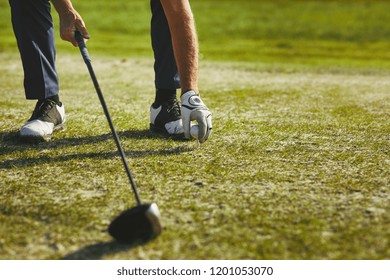 Closeup of a senior man placing a golf ball on a tee while standing on a golf course on a sunny day - Powered by Shutterstock