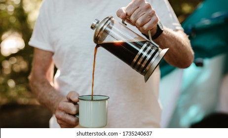 Close-up of a senior man pouring coffee in a mug at campsite. Male traveller having coffee at camping site. - Powered by Shutterstock