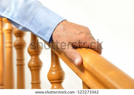 closeup of senior man using the wooden railing of stairs to go downstairs at his home