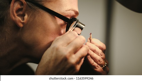 Closeup of senior woman goldsmith checking quality of a diamond. Female jeweler inspecting a gem through magnifying glass in workshop. - Powered by Shutterstock