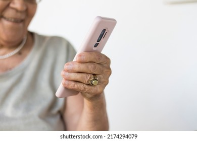 Close-up Of A Senior Woman Hand Holding A Mobile Phone. White Background. Copy Space. Old Woman Reading Message And Smiling.