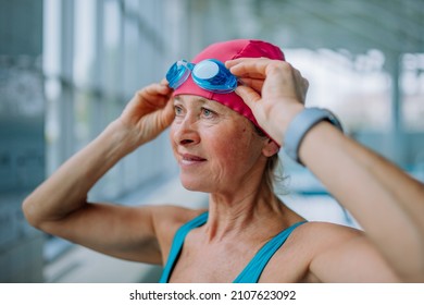 Close-up Of Senior Woman Putting On Goggles Before Swim In Indoors Swimming Pool.