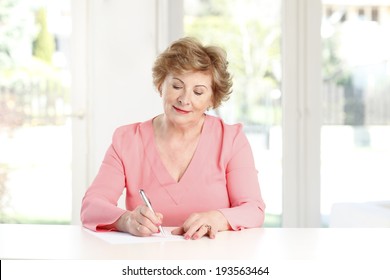 Close-up Of A Senior Woman Sitting At Desk And Making List. 