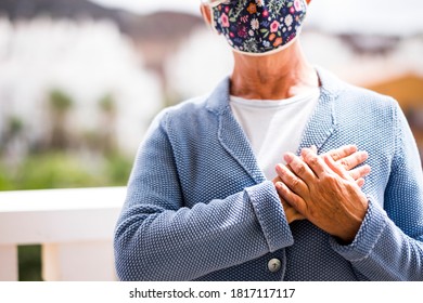 Closeup Of A Senior Woman Wearing Flowered Mask Greets With Hand Over The Heart. The New Greeting Recommended By The OMS World Health Organisation Due To The Coronavirus Covid-19