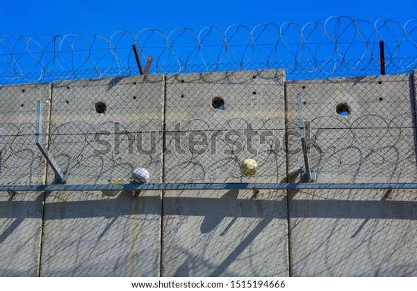 A closeup of\
the separation wall between Israel and Palestine. Two balls from\
kids in the West Bank caught in the barbed wire and fence. A symbol\
of division and segragation