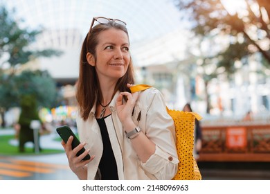 Close-up Sepia Styled Image Of Young Happy Smiling Student Girl With Smartphone In Hand In Fashionable Sunglasses Walking Outside In Sunny Summer Day Against Background Of Urban Landscape Exterior