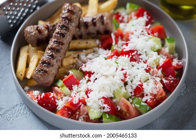Close-up of serbian shopska salad with grilled cevapi and fries in a grey plate, selective focus