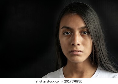 Close-up of a serious and beautiful black haired Latina woman wearing a white T-shirt on a black background. Copy space