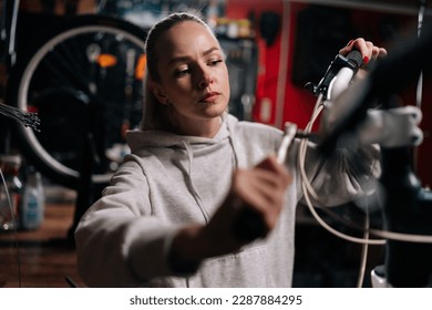 Closeup of serious blonde cycling mechanic female fixing bicycle handlebar with special tools working in bike repair shop with dark interior. Concept of professional maintenance of bicycle transport. - Powered by Shutterstock