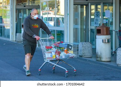 Closeup of a serious looking man with coronavirus protective mask pushing his shopping cart full of essentials. Routine scene outside grocery stores during COVID-19 pandemic in Tuscany, Italy 04/10/20