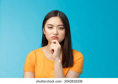 Close-up serious-looking suspicious female asian look disbelief, pondering, solving riddle, squinting hesitant disbelief, frowning suspect something wrong, thinking, focus stare, blue background