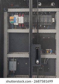 Close-up of a server rack door with a dark gray hexagonal perforated mesh. Inside, electronic components such as relays and colorful cables are visible.