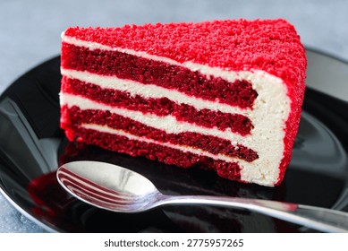 Closeup serving of a vibrant slice of red velvet cake with white cream cheese frosting on a black plate.