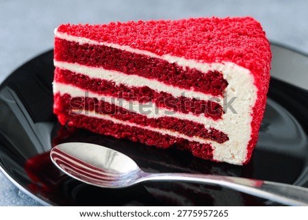 Closeup serving of a vibrant slice of red velvet cake with white cream cheese frosting on a black plate.