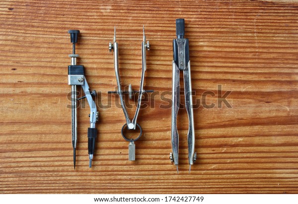 close-up of\
set of drawing tools including two metal dividers and one metal\
drawing compass isolated on wooden\
background