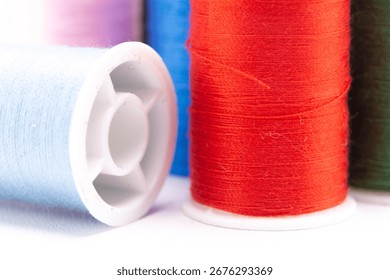 Close-up of several colorful thread spools, including red, blue, green, purple, and white, on a white surface.