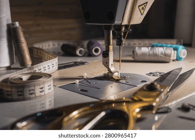 Close-up of a sewing machine with thread, measuring tape, scissors and sewing tools on a worktable. Tailoring, garment making and textile craft concept.