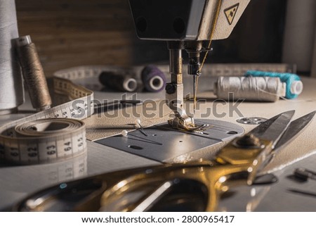 Close-up of a sewing machine with thread, measuring tape, scissors and sewing tools on a worktable. Tailoring, garment making and textile craft concept.