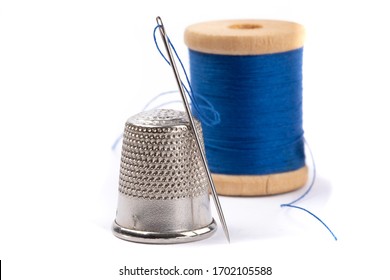closeup of a sewing thimble with a needle and blue thread isolated on white