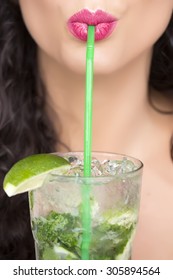 Closeup of sexual pretty brunette female face of girl with curly hair and pink lips drinking alcoholic mojito cocktail from mint soda light rum and lime with straw, vertical picture