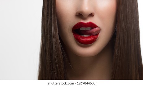 Close-up of sexy female lips with tongue. Clean skin and a clear lip contour are outlined with a fashionable red lipstick. White teeth and the beauty of a smile for stamotologii, spa or cosmetology