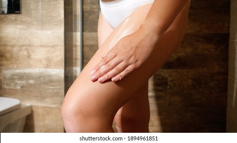 Closeup of sexy young woman applying body lotion or creme to remove cellulite and stretch marks on hips skin after taking a shower. Concept of female beauty, body care and healthcare.